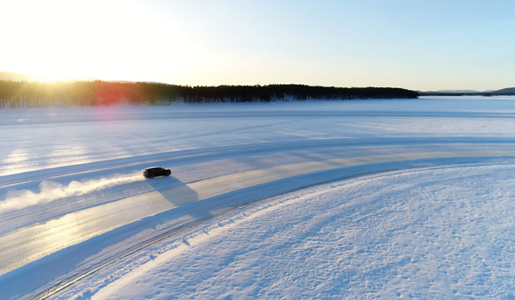 winter landscape with the sun in the left corner and a car driving on a snowy track