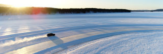winter landscape with the sun in the left corner and a car driving on a snowy track