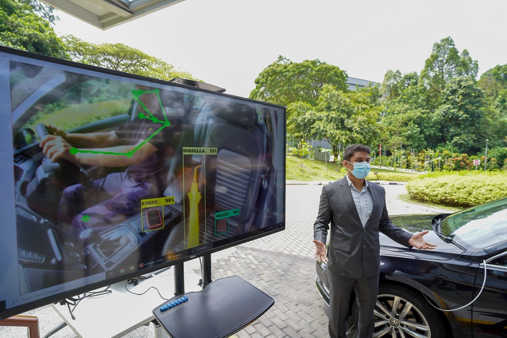 A person stands in front of a demo vehicle and explains new AI technologies on a large television screen at a media event at Nanyang Technological University in Singapore.