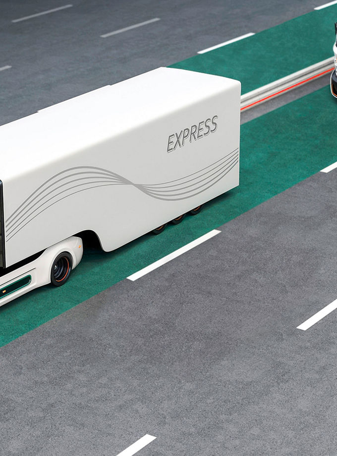 The photo shows two electric trucks in a separate lane for electric vehicles on a highway. AUMOVIO supports customers across the entire development lifecycle of electric heavy-duty vehicles – from the initial concept to industrialization and series production. 