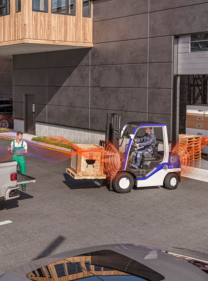 The picture shows a scene in front of a warehouse, where an electric forklift is loading a pickup truck with a large wooden case, warning bystanders with the AVAS acoustic warning system for electric vehicles.