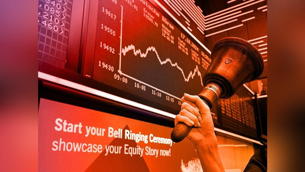 A hand bell is rung at the Frankfurt Stock Exchange in front of a large screen displaying DAX values.