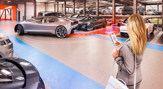 A woman uses her smartphone to automatically move a futuristic vehicle out of its parking space in a parking garage.