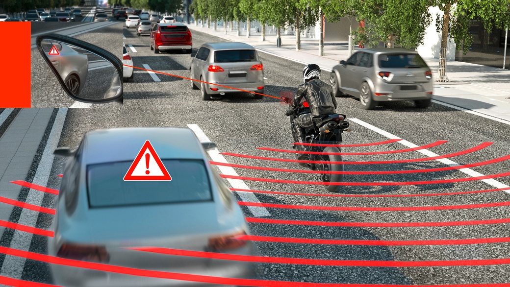 The image shows a traffic situation with heavy traffic. A vehicle is passing a motorcyclist on the left; the motorcycle is scanning the area behind it using radar sensors and displaying a warning message about the car approaching from behind in the motorcycle's side mirror.