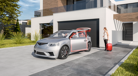 Modern silver sedan parked in front of a contemporary house with a large black garage door. The car’s front passenger door and rear hatch are open, highlighted in red, showcasing advanced body and actuator control features. A person stands nearby with a red suitcase, ready to load or unload luggage. The setting includes a clean gray driveway, green landscaped grass, and a stylish building with white walls, wooden accents, and large glass windows under bright daylight.
