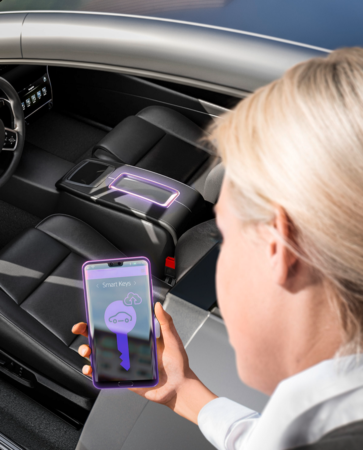 Image of a woman looking at her smartphone in front of an open car door. The smartphone display shows a digital key related to the topic of convenient smart device-based access. The digital access solution CoSmA allows the driver to access and start the vehicle by using a digital key on a smart device. Offering a completely new user experience, this system meets the demands of the mobile society with a new level of comfort, security, and new mobility functionalities.