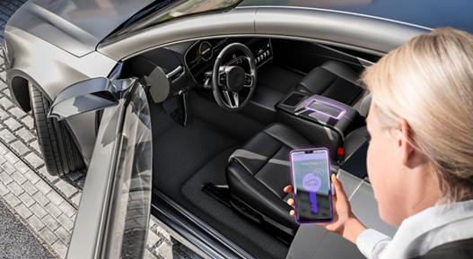 Image of a woman looking at her smartphone in front of an open car door. The smartphone display shows a digital key related to the topic of convenient smart device-based access. The digital access solution CoSmA allows the driver to access and start the vehicle by using a digital key on a smart device. Offering a completely new user experience, this system meets the demands of the mobile society with a new level of comfort, security, and new mobility functionalities.