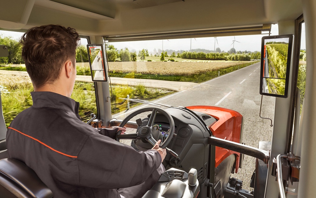 Tractor cabin view featuring digital mirror displays for enhanced rear and side visibility on rural road.