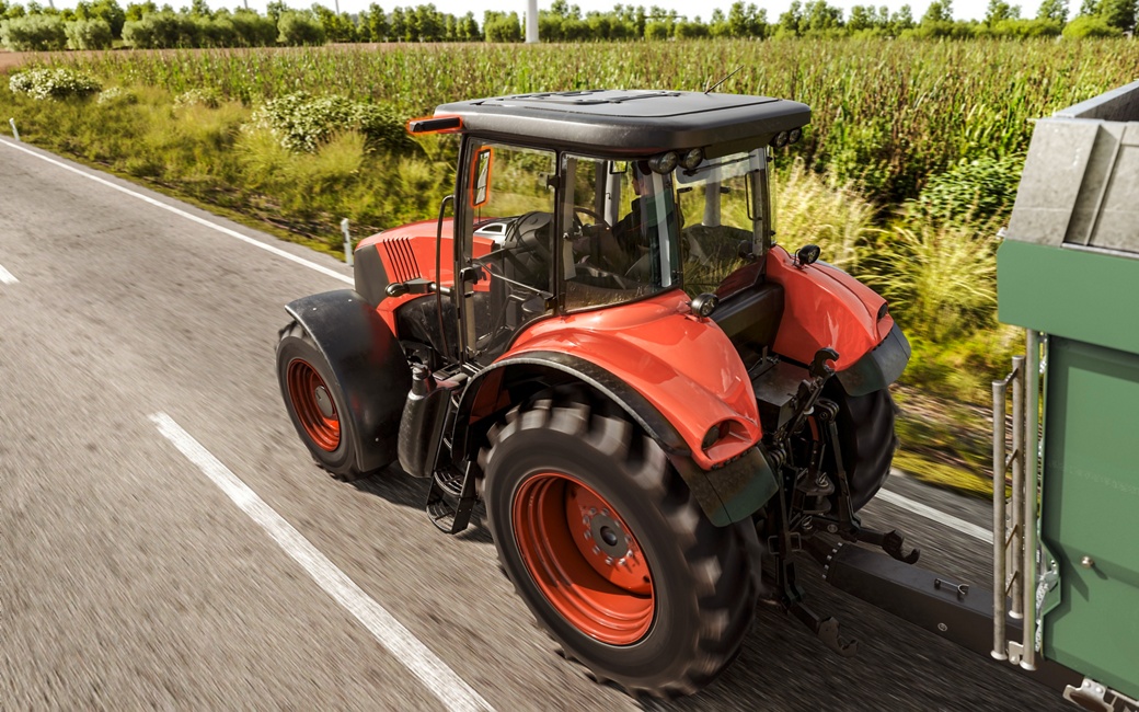 Roter Traktor mit Anhänger auf einer Landstraße, aufgenommen aus der Rückansicht.