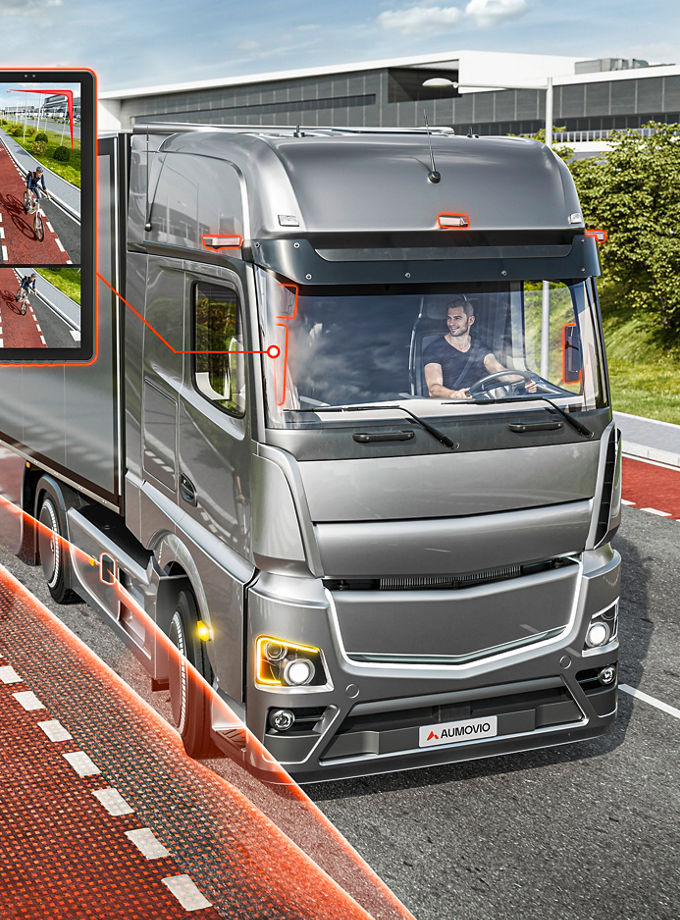 Modern truck equipped with a digital mirror system detecting a cyclist in the blind spot, highlighted with red safety zones on a multi-lane road.
