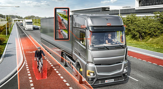 Modern truck equipped with a digital mirror system detecting a cyclist in the blind spot, highlighted with red safety zones on a multi-lane road.