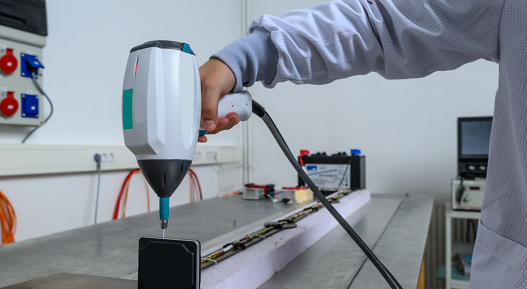 The picture shows a person using a testing device during electrical testing. AUMOVIO provides a globally aligned framework for validating the performance, reliability, and compliance of complex electronic systems across diverse industries.
