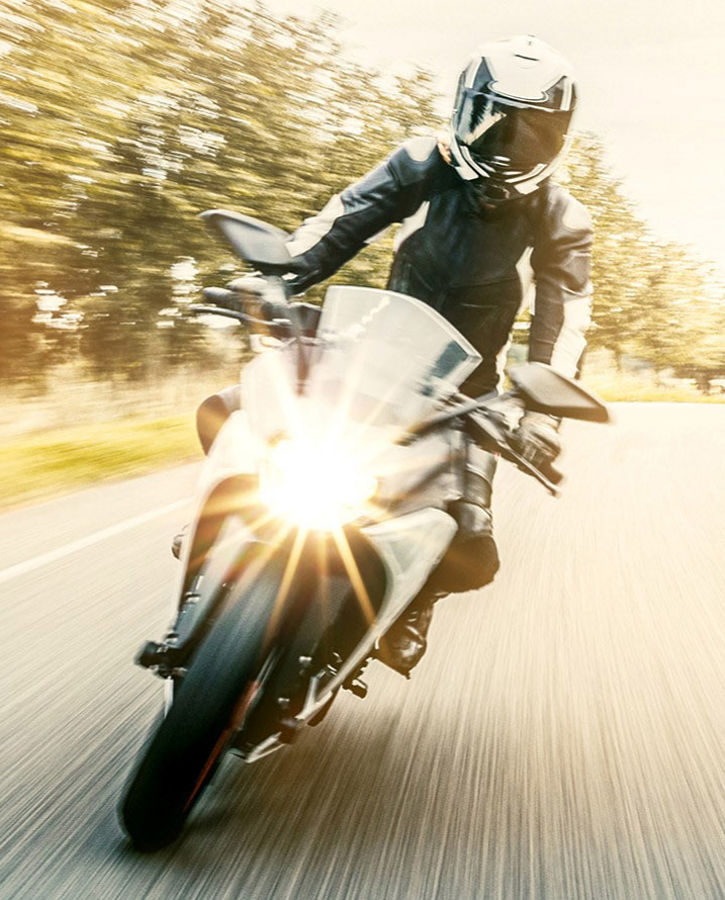 Motorcycle rider on a bright road with motion blur effect, wearing protective gear, with sunlight illuminating the scene, representing e-mobility for two-wheelers.