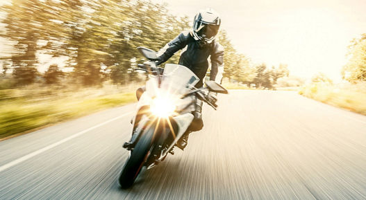 Motorcycle rider on a bright road with motion blur effect, wearing protective gear, with sunlight illuminating the scene, representing e-mobility for two-wheelers.