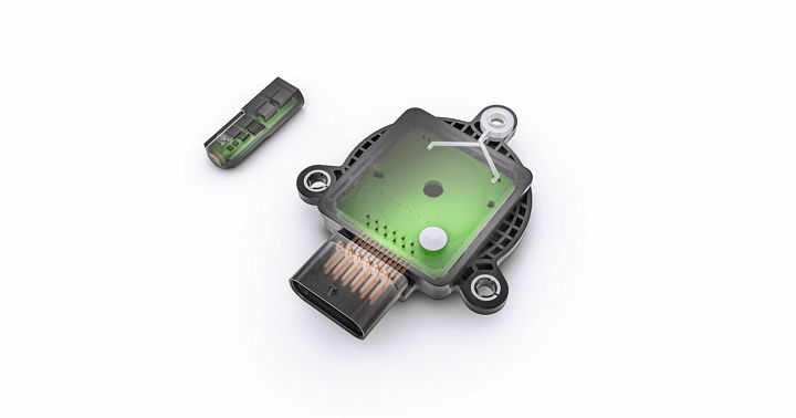 Image showing a rotor position sensor with its cover removed, revealing internal green circuit board and electronic components. A separate small sensor module is placed next to it, illustrating the advanced design for precise rotor position detection in electric drive systems.