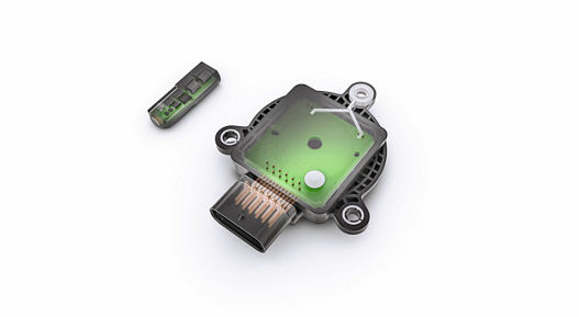 Image showing a rotor position sensor with its cover removed, revealing internal green circuit board and electronic components. A separate small sensor module is placed next to it, illustrating the advanced design for precise rotor position detection in electric drive systems.