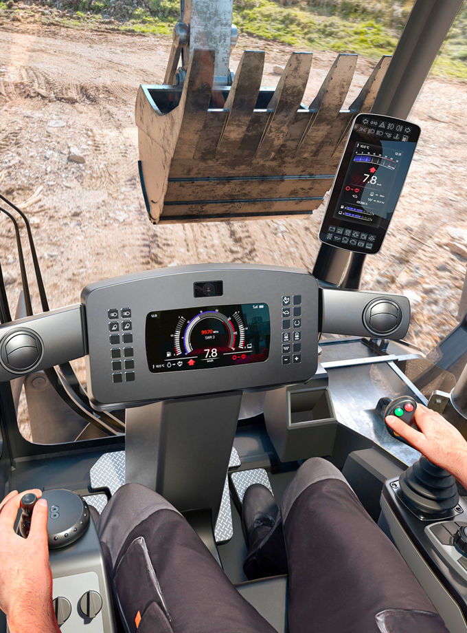 The image shows the interior of a digger cab while the driver is operating the vehicle, with a focus on the instrumentation display. AUMOIVIO's display solutions offer premium image quality thanks to high-resolution, full-color HD-displays and special anti-reflection, anti-glare and anti-fog surface treatments.