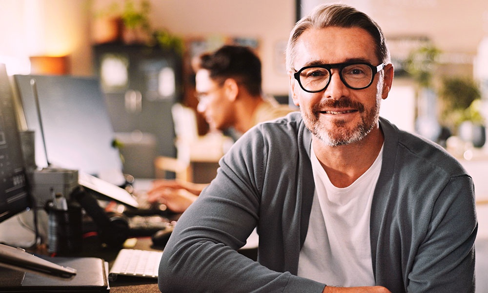 Eine Person sitzt an einem Schreibtisch in einer modernen Büroumgebung mit Computermonitoren und verschwommenen Aktivitäten im Hintergrund.