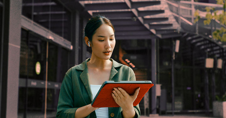 A woman in a green blazer uses a digital tablet in a modern outdoor business environment, representing organized media coordination and streamlined press contact management.