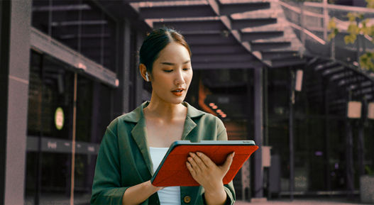 A woman in a green blazer uses a digital tablet in a modern outdoor business environment, representing organized media coordination and streamlined press contact management.