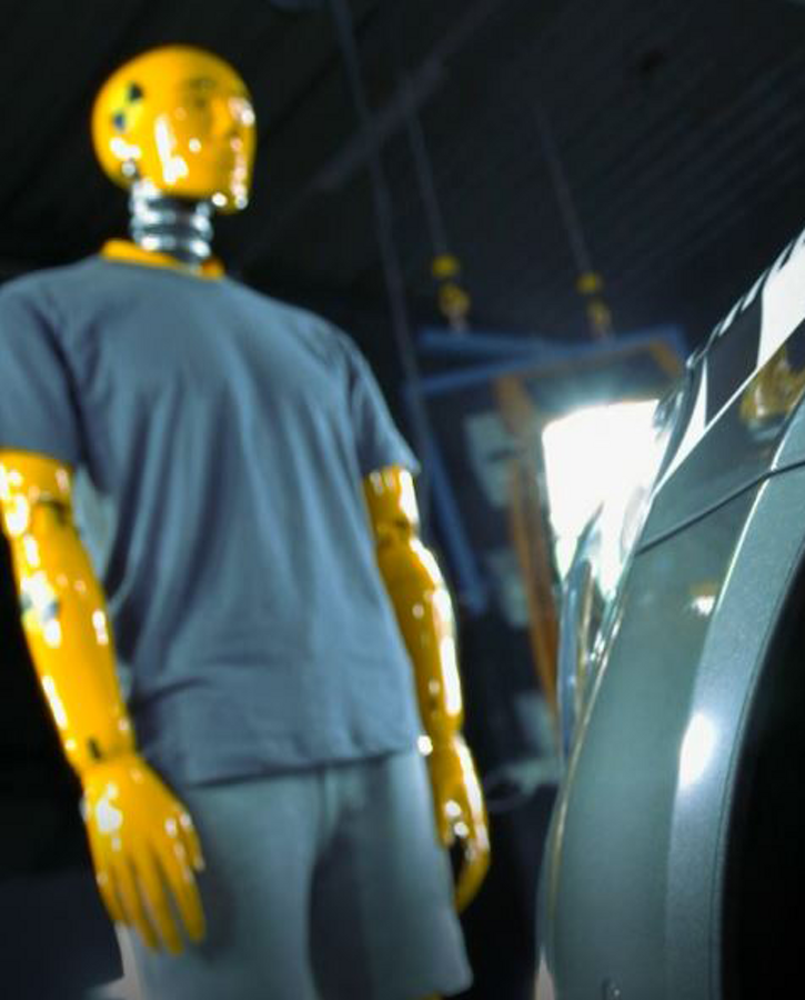 Image of a crash test dummy standing in front of a test vehicle in a proving ground facility