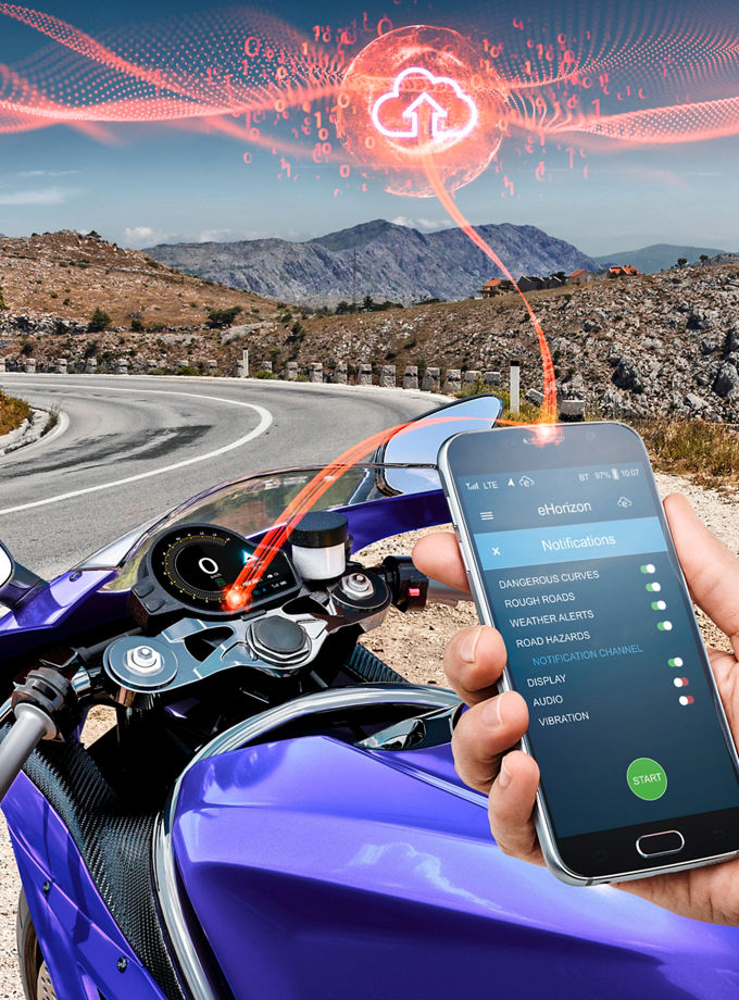 Image of a motorcyclist sitting on his motorcycle and holding his smartphone in his hand. An orange line extends from the smartphone to a cloud in the sky and to the motorcycle display. Aumovio offers a range of high-performance instrument displays tailored for motorcycles, designed to offer maximum flexibility. It employs automotive-grade technology with optical bonding for crystal-clear visuals.