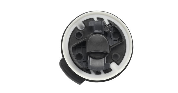 Close-up view of a round automotive sensor with a black inner structure and a white outer ring. The component features multiple mounting points and a central locking mechanism, designed for integration in vehicle safety systems.