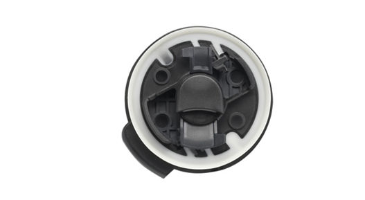 Close-up view of a round automotive sensor with a black inner structure and a white outer ring. The component features multiple mounting points and a central locking mechanism, designed for integration in vehicle safety systems.