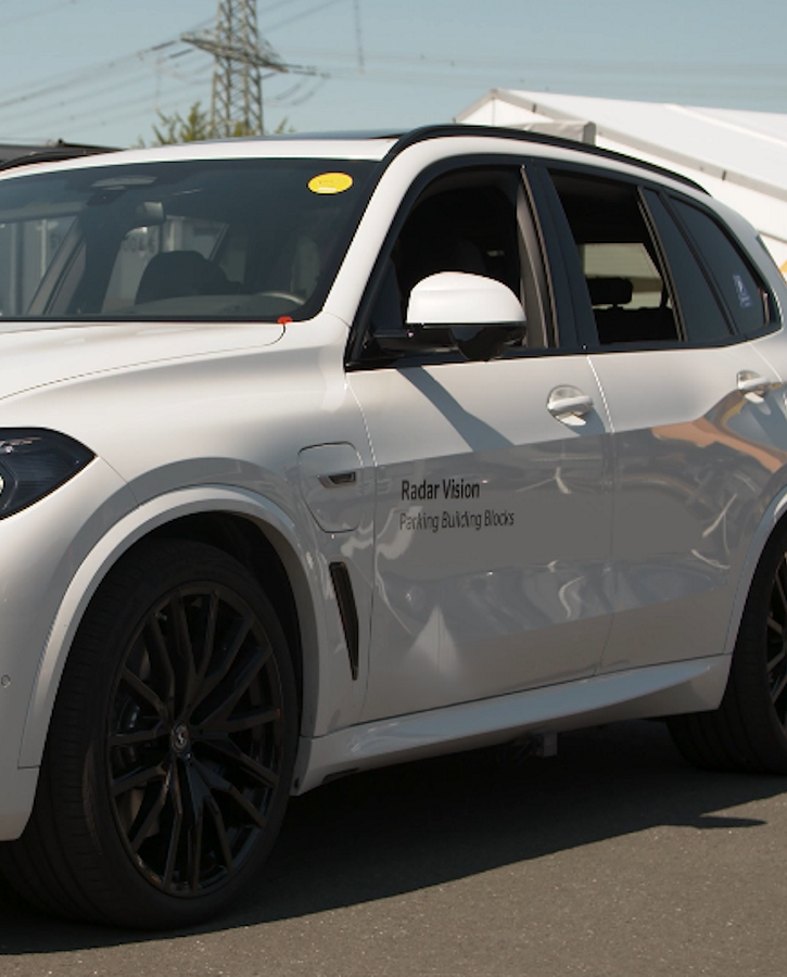 White SUV equipped with radar vision technology for automated parking, displayed outdoors at a tech showcase with visible branding on the front door.
