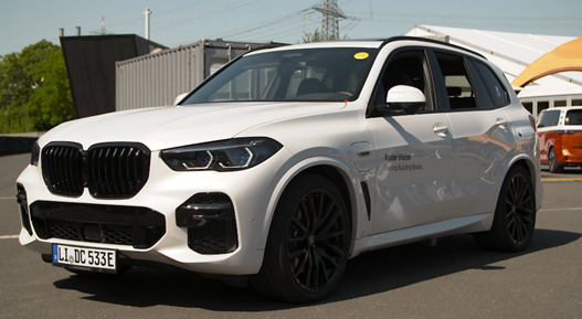 White SUV equipped with radar vision technology for automated parking, displayed outdoors at a tech showcase with visible branding on the front door.