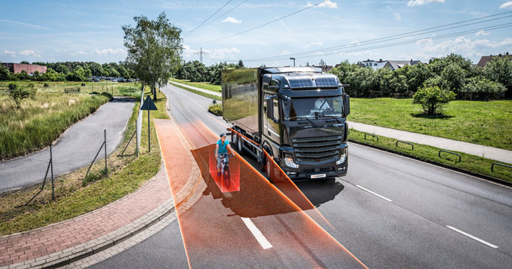 Large truck equipped with right-turn assist system detecting a cyclist in the blind spot, highlighted by orange safety zones on the road.