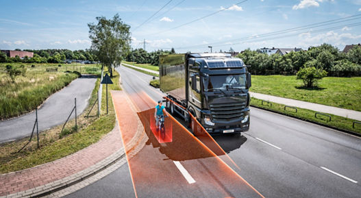 Large truck equipped with right-turn assist system detecting a cyclist in the blind spot, highlighted by orange safety zones on the road.