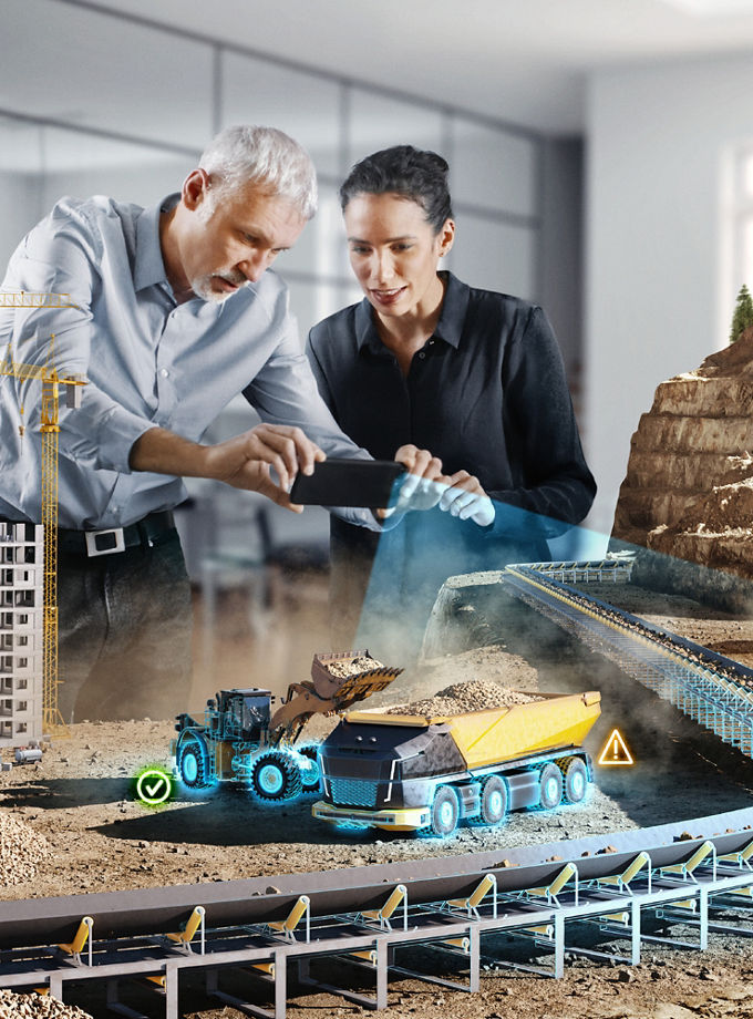 The image shows a large construction site model. Two people are scanning parts of the construction site model with a smartphone. The scanning is represented by light blue beams. The scene refers to AUMOVIO's sensor portfolio. Our advanced automotive sensors, which are innovative and safe, are driving the automotive industry forward. From tire pressure monitoring systems to sensors for electric vehicles, our products are designed to meet the requirements of modern vehicles.