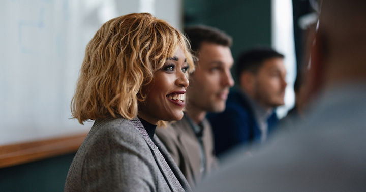 Close up shot of a beautiful smiling businesswoman, sitting at her desk at the office, looking down and using her laptop computer.