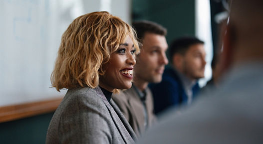 Close up shot of a beautiful smiling businesswoman, sitting at her desk at the office, looking down and using her laptop computer.