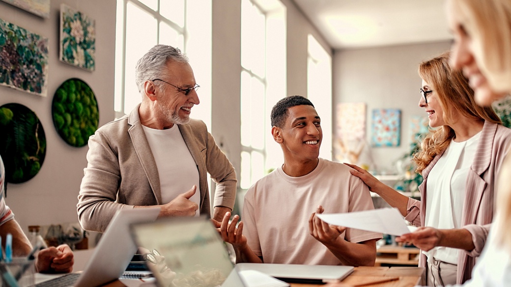 A diverse group of professionals collaborating in a bright and creative office space. They are engaging in a discussion with smiles, sharing ideas, and working together as a team in an inspiring and supportive environment.