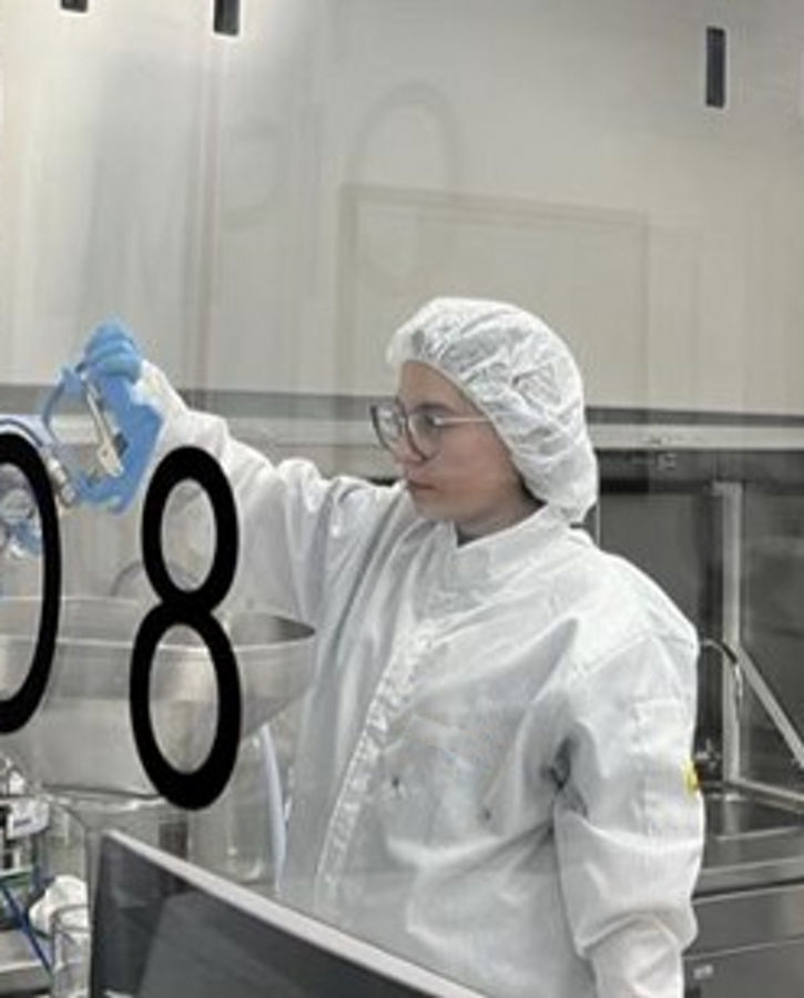 A photo of a person behind a large glass window in a laboratory. Technical cleanliness is a specialized methodology used to assess and control particulate contamination in components and systems, particularly in industries where even microscopic debris can compromise performance, reliability, or safety.