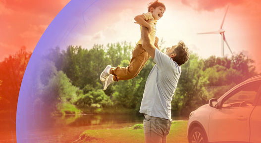 A person lifts a child joyfully in a scenic outdoor setting with lush greenery, a wind turbine in the background, and a car parked nearby, symbolizing family moments and sustainable living.
