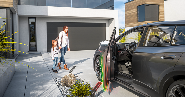 Modern car parked in front of a contemporary house with the driver’s door open, highlighted by green and red visual effects representing power door technology. Decorative landscaping and clean driveway complete the scene.